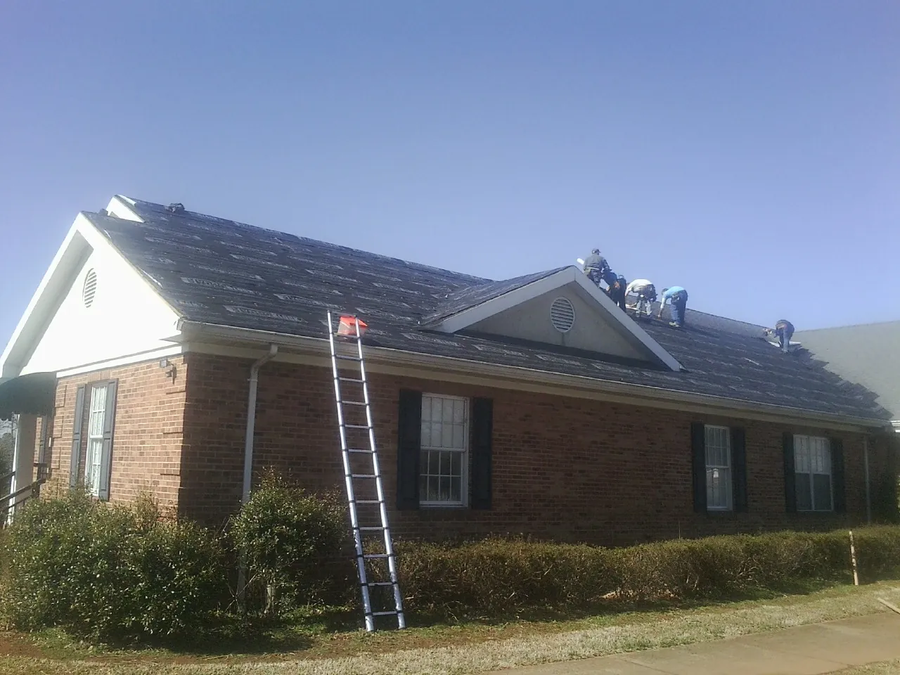Crew tearing shingles off a brick ranch roof with a ladder set — Emergency Roof Repair work by our crew in Page