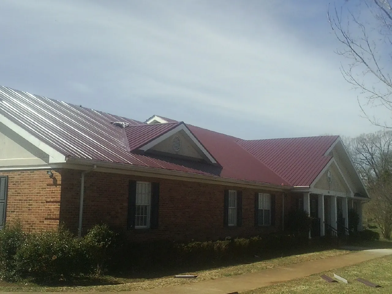 Red metal roof with gabled entries on a long brick building, from a Hail Damage Roof Repair job in Page