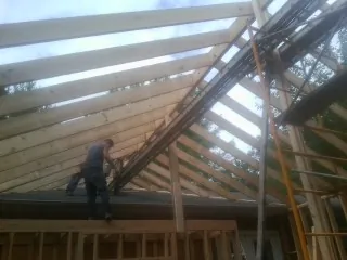 Rafters going up over a new addition with a worker on the wall in Page