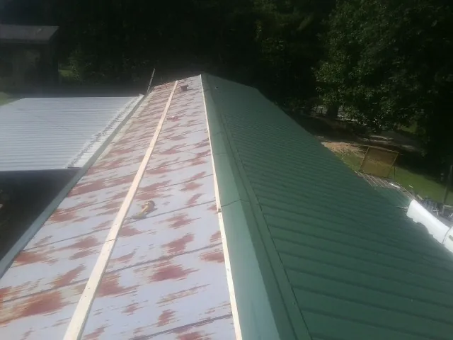 Old rusted panels beside newly installed green metal roofing — Wind Damage Roof Repair by Roofing Brothers in Page