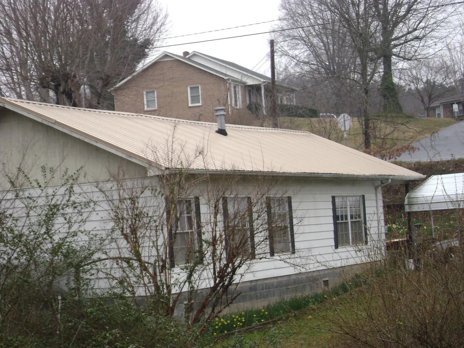 Tan metal roof on a white sided house set into a hillside — Commercial Roofing by Roofing Brothers in Page